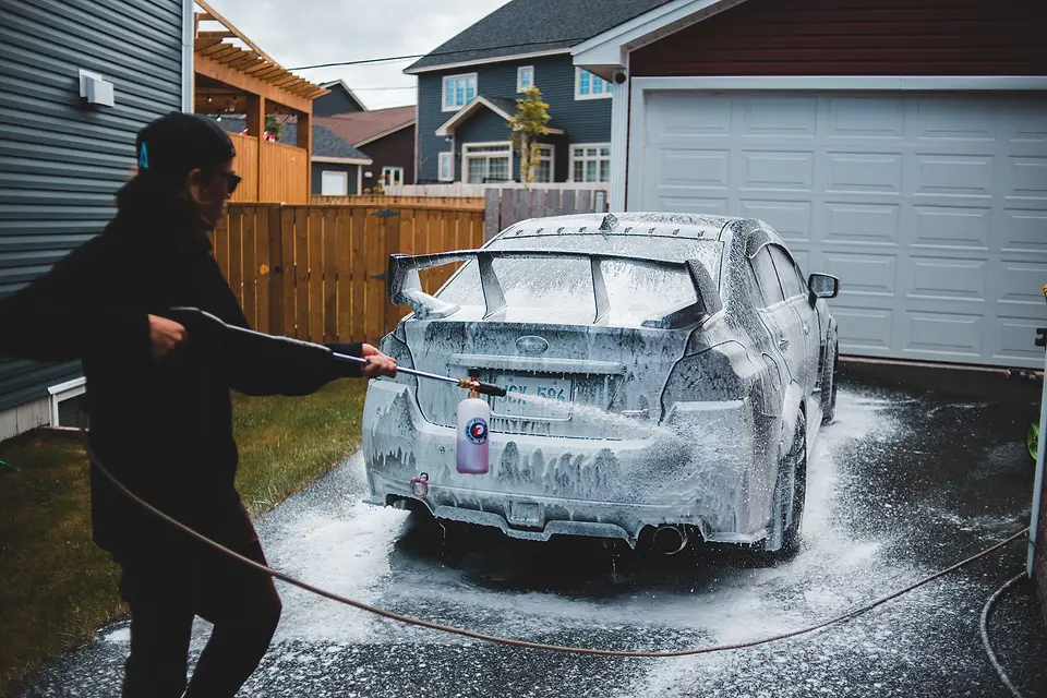 Detailer foaming a car in front of a garage at home