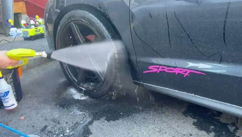 Rinsing a black wheel with a pressure sprayer before brushing